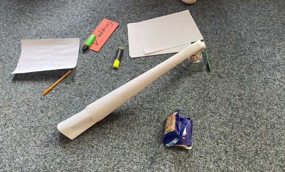 Zu sehen ist ein Turm, der aus verschiedenen Materialien zusammengebaut wurde. In diesem Fall hauptsächlich Papier und Schokolinsen.