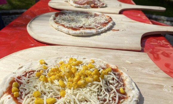 Zu sehen sind selbstgemachte Pizzen, bevor sie in den Steinofen kommen. Die jungen menschen haben sie selbst belegt. Mit Tomatensauce, Mais, Salami und vielem mehr. 